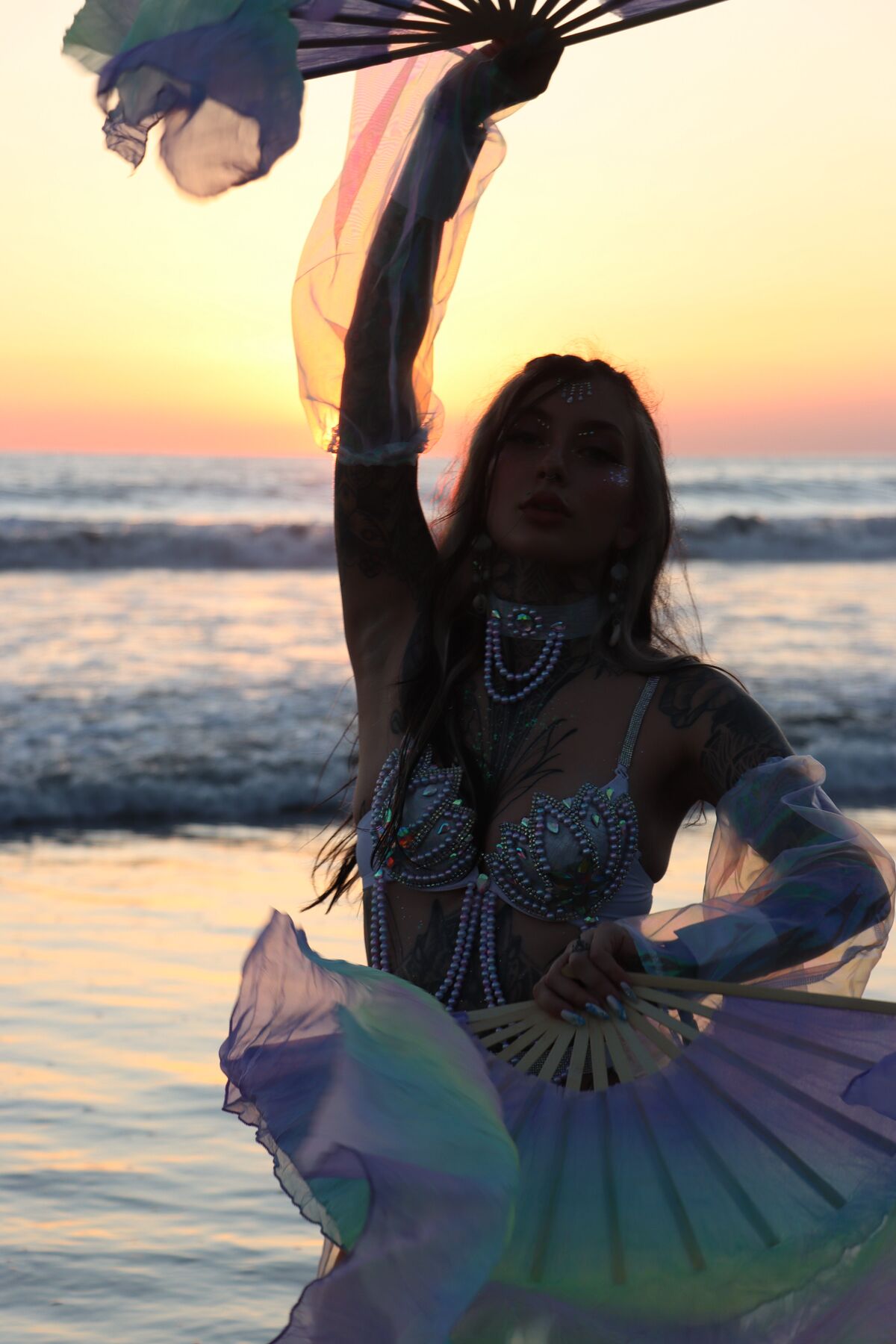 Silhouette raising a silk fan against the sun setting over the ocean